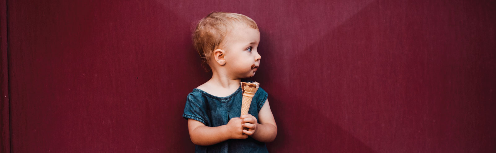 Child holding ice cream cone in front of a burgundy wall.