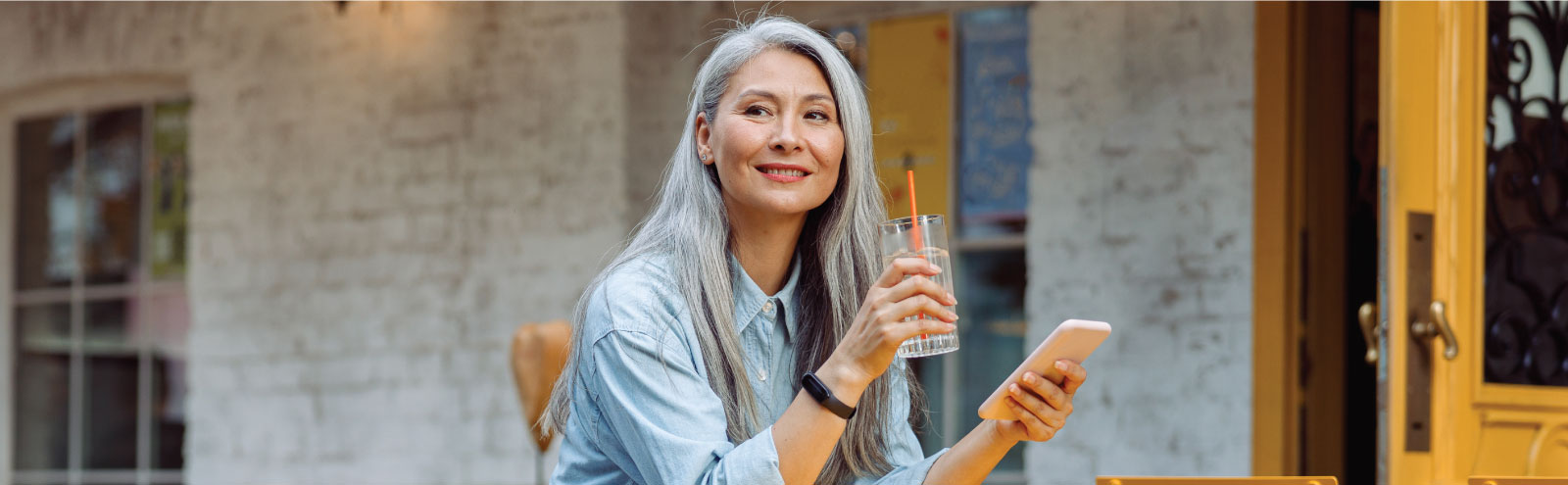 Grey-haired woman at an outdoor cafe holding a water and her phone.